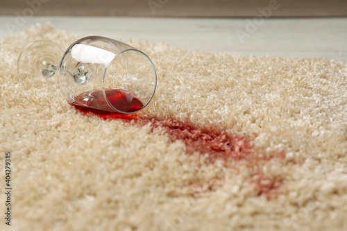 Overturned glass and spilled red wine on soft carpet, closeup