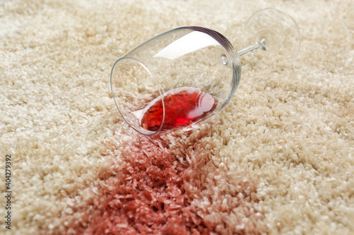 Overturned glass and spilled red wine on soft carpet, closeup
