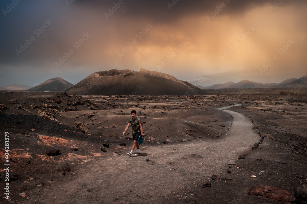Young man walks along the path of El Cuervo volcano in Timanfaya National Park at sunset. Lanzarote. canary islands