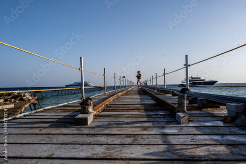 a woman walks along a long bridge over a coral reef into the sea