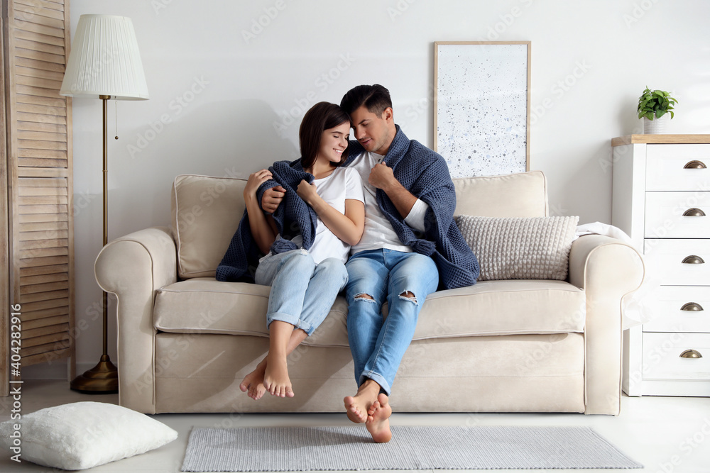 Obraz premium Happy couple in love covered with warm dark blue plaid sitting on sofa at home