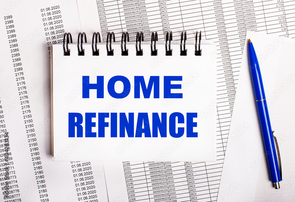 On the table are charts and reports, on which lie a blue pen and a notebook with the word HOME REFINANCE On the table are charts and reports, on which lie a blue pen and a notebook with the word HOME REFINANCE