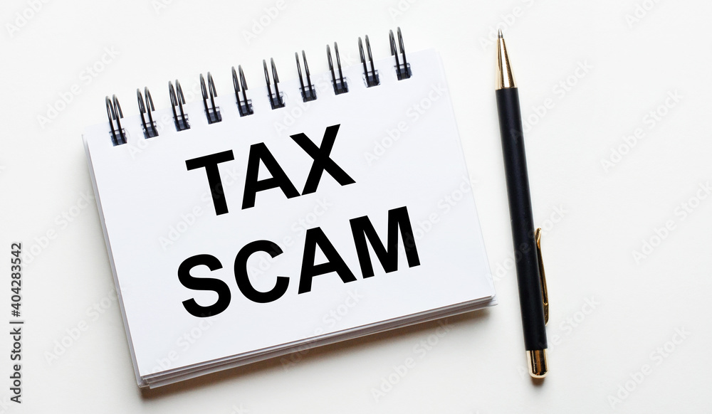 On a light background, a white notebook with the words TAX SCAM and a pen. On a light background, a white notebook with the words TAX SCAM and a pen.