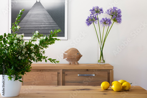 living room interior with table, lemons and vase of white myrtle flowers, furniture with decoration and vase of purple agapantus