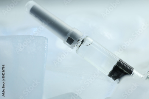 Syringe with COVID-19 vaccine on ice cubes, closeup