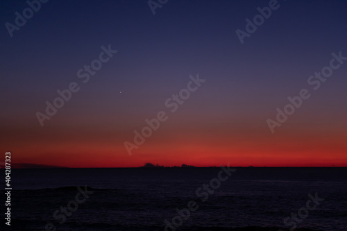 Vivid red blue gradient sky over the ocean at dusk with dark clouds on the horizon and star visible