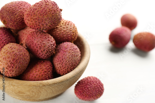 Fresh ripe lychees in bowl on white wooden table, closeup. Space for text