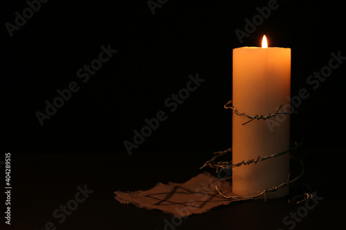 Fabric with star of David, barbed wire and burning candle on black background, space for text. Holocaust memory day photo