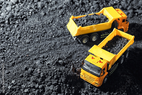 Toy tipper trucks with coal in field. Space for text