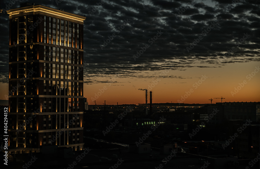 City skyscraper at sunset, on the horizon of the factory pipe, the windows reflect the light from the sunset. Beautiful lighting of the building. City skyscraper at sunset, on the horizon of the factory pipe, the windows reflect the light from the sunset. Beautiful lighting of the building.