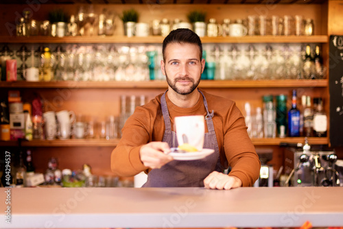 Smiling coffee shop owner businessman standing behind the counter in the cafe and holding a cup of tea in her hand. 