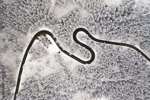 Curved S-shaped road in the winter forest aerial view. Empty winding road surrounded by high pine trees.  © vladim_ka
