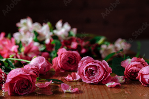 Fresh pink roses flowers with petals an leaves on the wooden table and dark black background. Still life