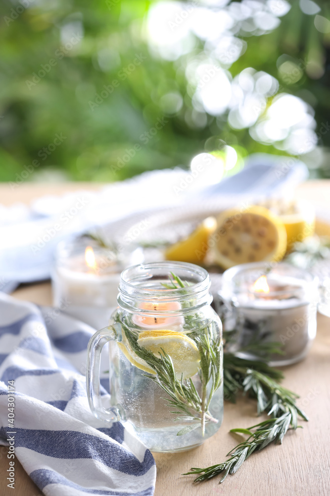 Mason jar with slice of lemon, fresh rosemary and water on wooden table outdoors. Natural homemade repellent