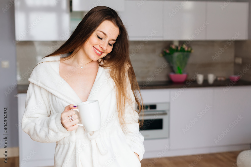 Young attractive girl drinking morning coffee from a large white Cup, smiling, morning portrait. Copy space. Young attractive girl drinking morning coffee from a large white Cup, smiling, morning portrait. Copy space.