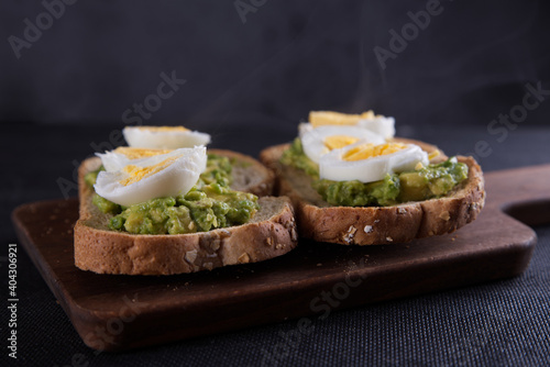 Sandwich prepared with oat toast, avocado and boiled egg, with dark backgrounds.