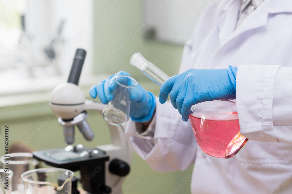 Scientist pouring pink substance from one flask to another in a laboratory Scientist pouring pink substance from one flask to another in a laboratory