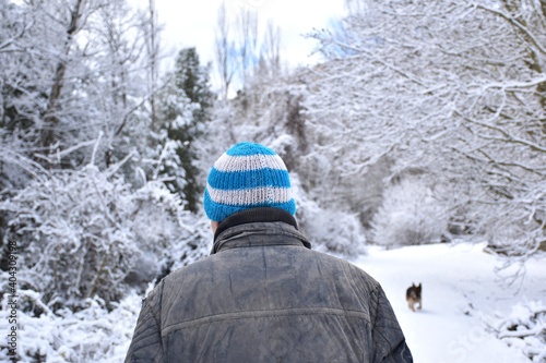 Man in old black jacket and blue and white woolen hat walking on snow-filled country road. Temporary Filomena.