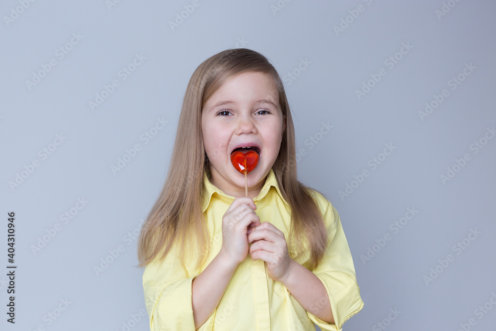 valentine's day caucasian child holding a lollipop heart over grey background. Funny face. Selective focus. valentine's day caucasian child holding a lollipop heart over grey background. Funny face. Selective focus.
