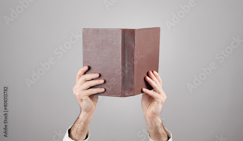 Male hands holding book on grey background.
