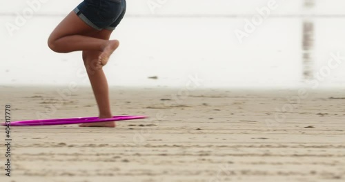 Woman twirling hula hoop using one leg on a sandy beach. Girl doing fitness activity by the sea. High quality 4k footage