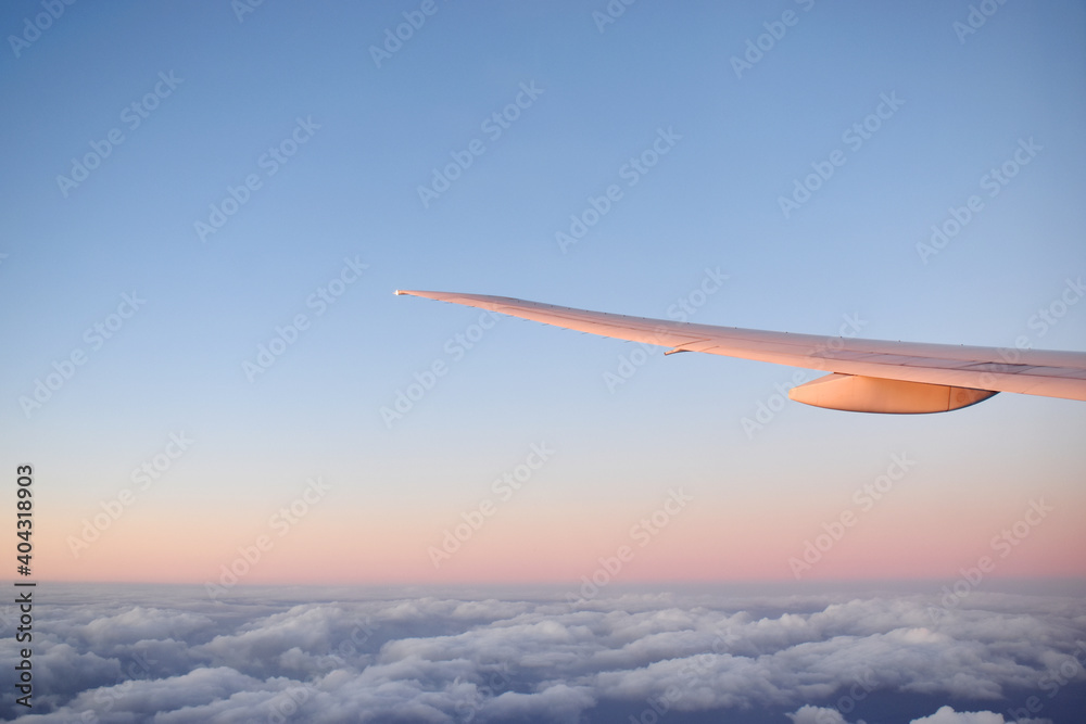 Fototapeta premium Aircraft wing above cloudscraper with horizon of pink and blue sky,view from airplane window.