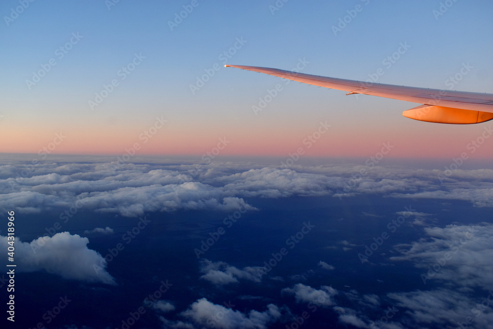 Aircraft wing above cloudscraper with horizon of pink and blue sky,view from airplane window.