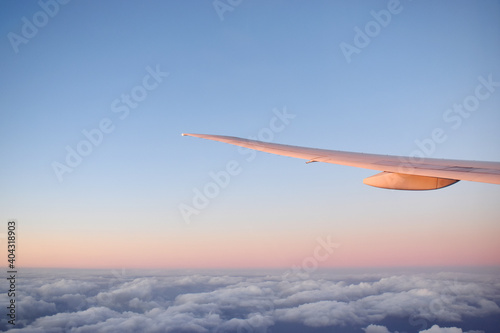 Aircraft wing above cloudscraper with horizon of pink and blue sky,view from airplane window.