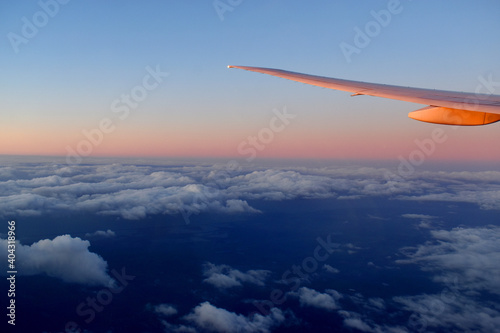 Aircraft wing above cloudscraper with horizon of pink and blue sky,view from airplane window.