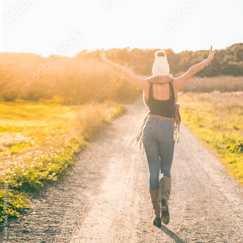 girl walking down a dirt road at sunset with open arms. She is on her back and the light is golden.