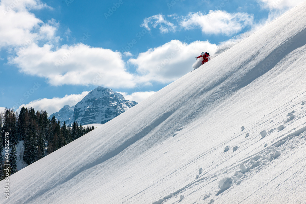 Stock picture of a freeride skier that is skiing fast downhill in deep powder snow. Big mountains and blue sky in the background. The location is Lofer in Austria