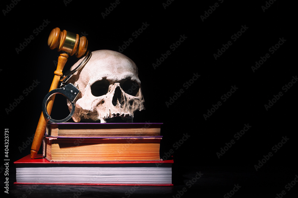 Legal law, justice and murderment concept. Wooden judge gavel hammer on human skull and books with handcuffs against black background. Free space. Legal law, justice and murderment concept. Wooden judge gavel hammer on human skull and books with handcuffs against black background. Free space.