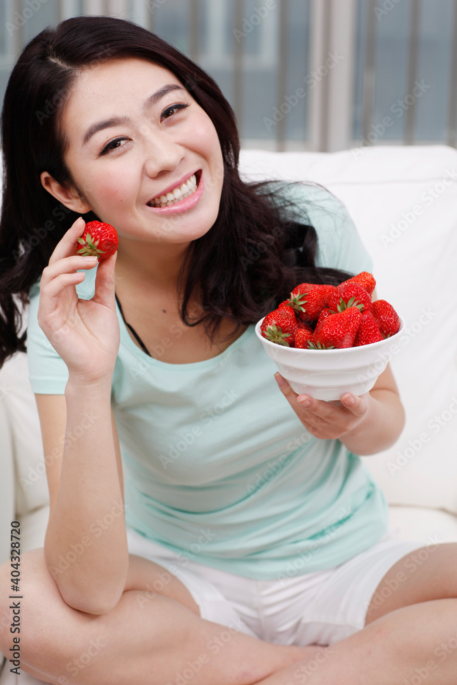 Young woman sitting on a couch,holding a bowl of strawberries Young woman sitting on a couch,holding a bowl of strawberries