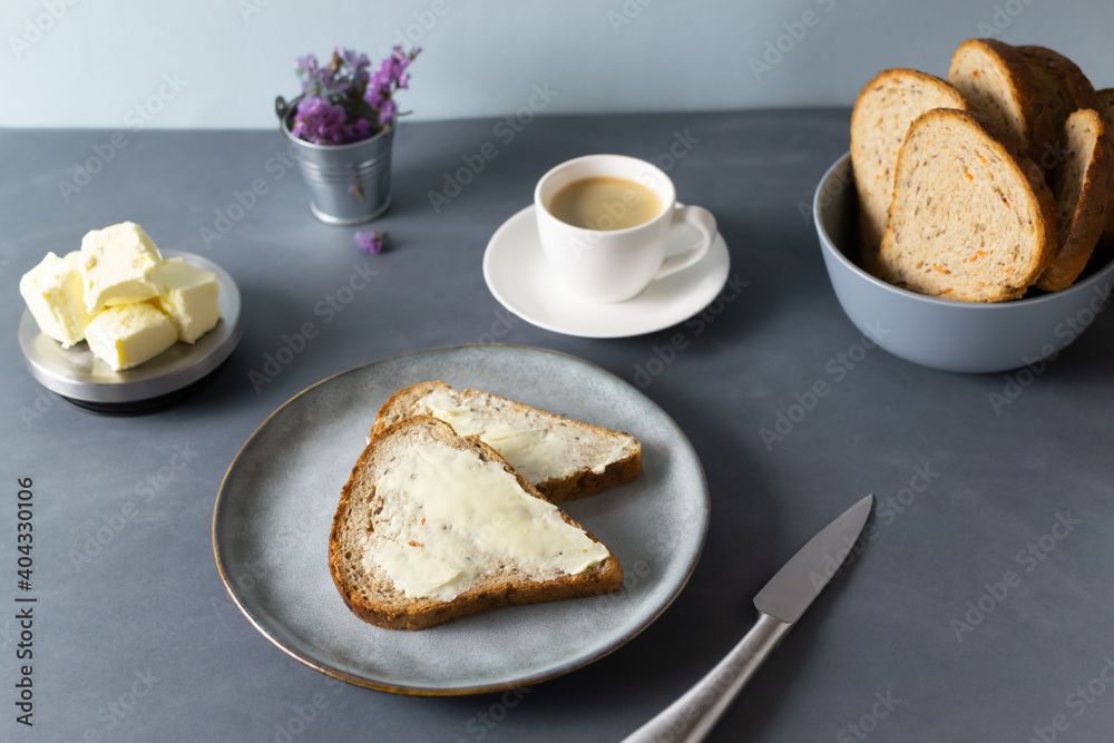 Homemade carrot bread with bran, butter and a cup of coffee on a gray background. Healthy nutrition concept. Copy space. Homemade carrot bread with bran, butter and a cup of coffee on a gray background. Healthy nutrition concept. Copy space.