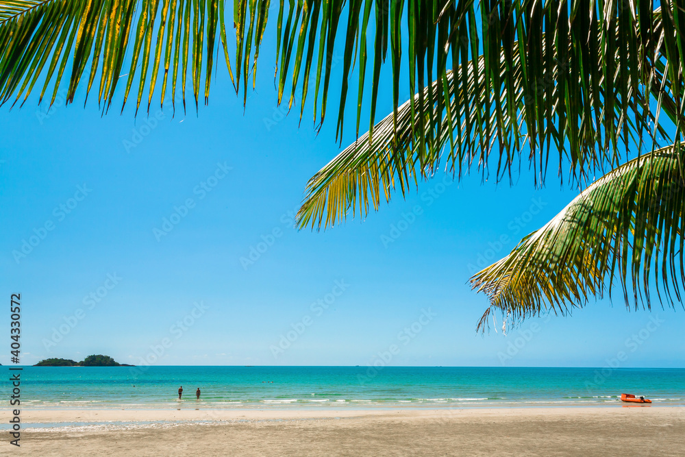 Naklejka premium Beautiful beach and blue color ocean waves under green palm leaves. Natural view under tropical sun. Holidays in tropical country