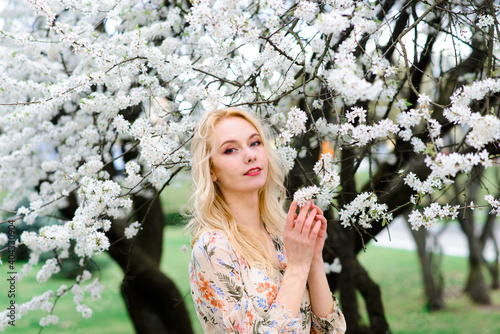 Waist up portrait of young smiling woman with blond hair near blossoming plum tree