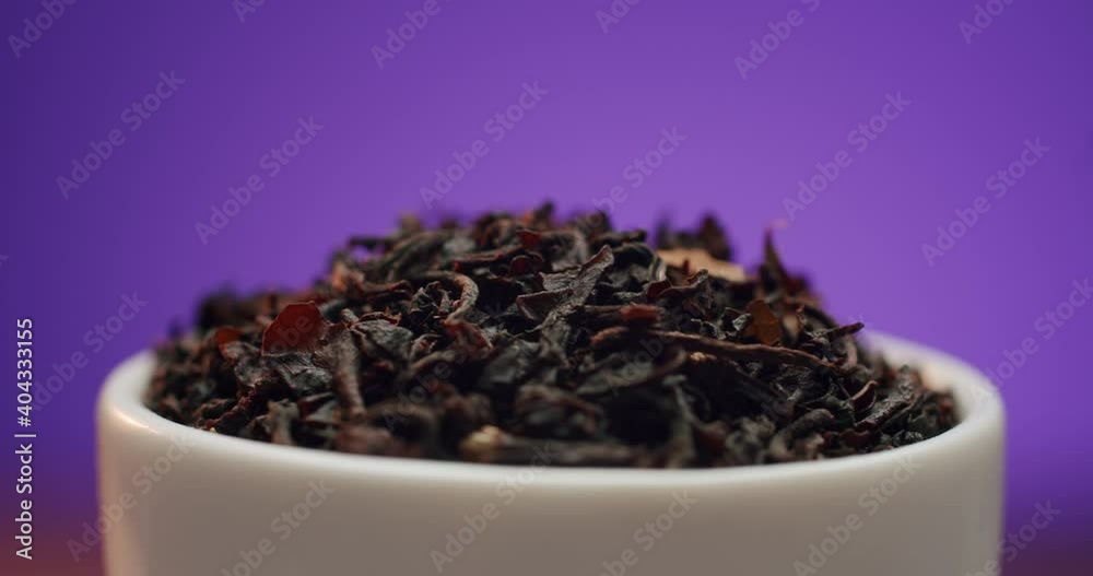 Macro shot of pure large frush ceylon leaf black tea rotating in small bowl on purple background. Copy space, place for text. Extreme close up shot Macro shot of pure large frush ceylon leaf black tea rotating in small bowl on purple background. Copy space, place for text. Extreme close up shot