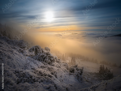 Scenic landscape with a view from a mounatin range to the valley filled with low clouds and fog during temperature inversion,snow,rime,clouds,spruce trees,sun.Jeseniky mountains.Czech republic. .