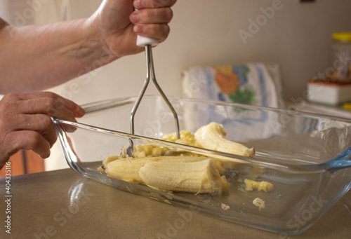 woman hands preparing mashed banana for banana cake, banana bread or diet food in the glass bowl in kitchen.. Close up.