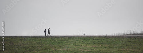 a couple walking in the distance silhouetted against a plain grey sky and green meadow 