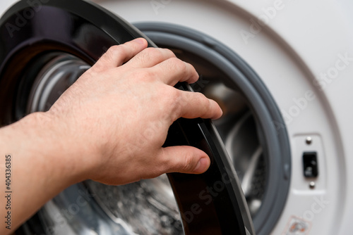Man's hand opens the door of the washing machine