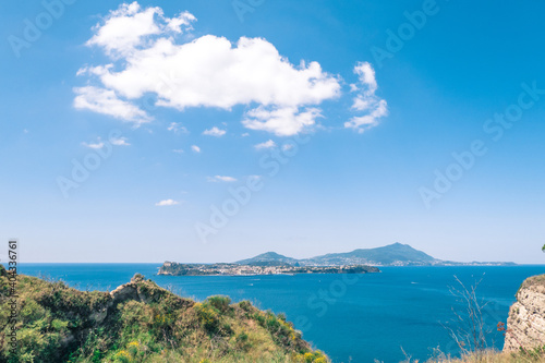 view in the gulf of Naples from Monte di Procida with the islands of Procida and Ischia in the background and vegetation in the foreground, under a blue sky with cloud