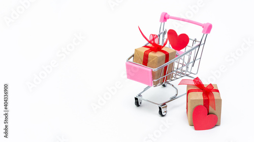 Small grocery cart with gift boxes on white background. Give gifts with love on Valentine's Day, Christmas and birthday. Shopping online. Holiday sales and discounts. Retail and wholesale purchases.