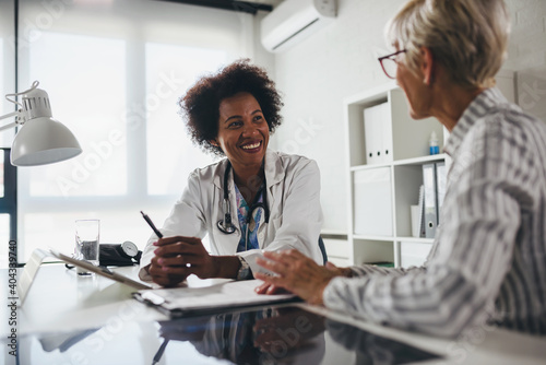 A female black ethnicity doctor sits at her office and talking with elderly female patient