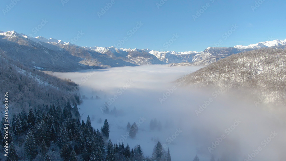 DRONE: Dense fog covers the valley under the spectacular snowy mountain range.
