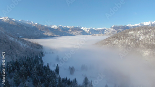 DRONE: Dense fog covers the valley under the spectacular snowy mountain range.