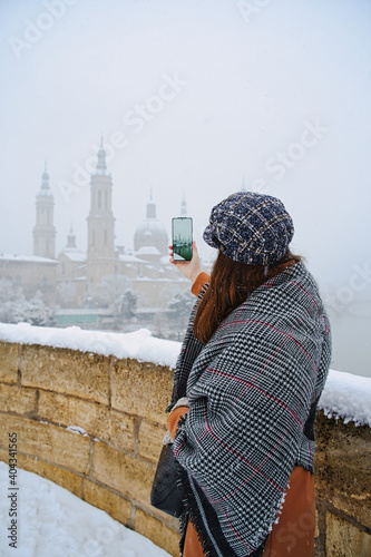 woman photographing "basilica del pilar" in zaragoza while it snows