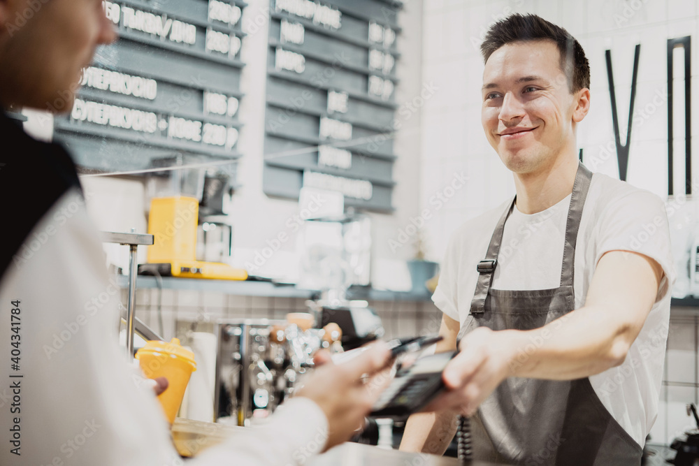 sells coffee employee staff of restaurant cafe bartender with dark hair. a man of Caucasian appearance in a work apron and a white T-shirt. sells coffee employee staff of restaurant cafe bartender with dark hair. a man of Caucasian appearance in a work apron and a white T-shirt.