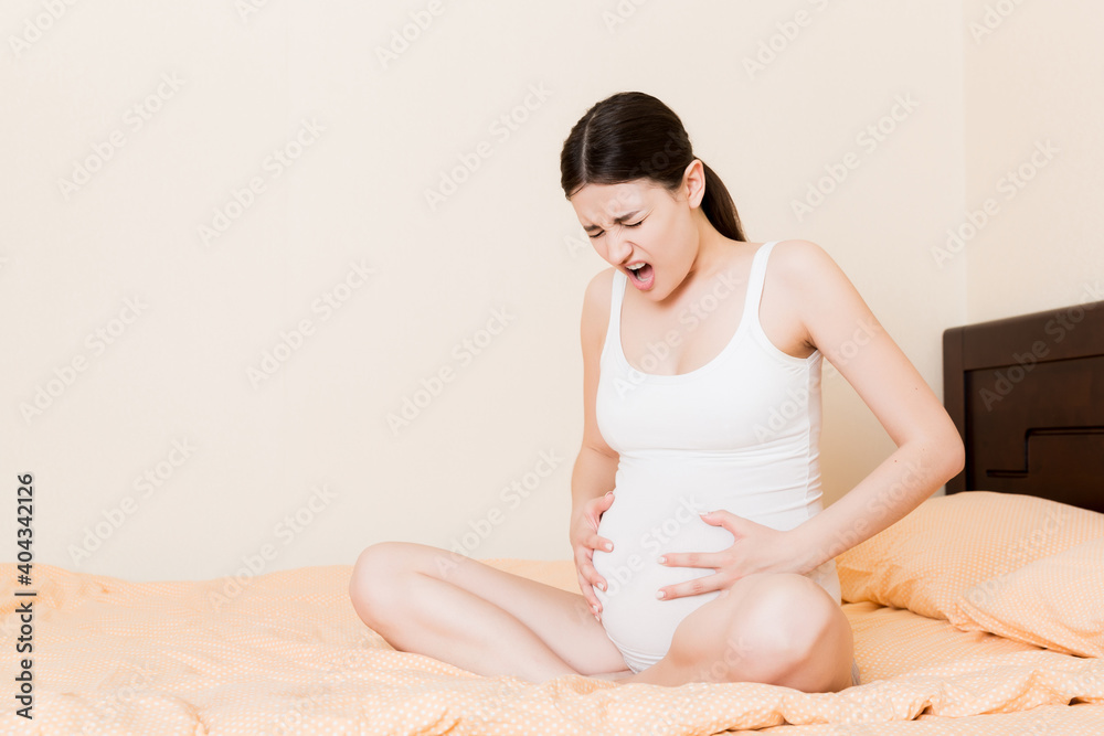 Pregnant Lady Having Massaging Lower belly Sitting On Sofa Indoor. Pregnancy Problems Concept. Maternity healthcare Pregnant Lady Having Massaging Lower belly Sitting On Sofa Indoor. Pregnancy Problems Concept. Maternity healthcare