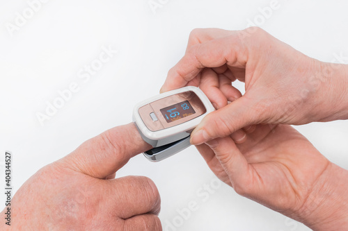 The hand of an elderly man inserted a finger into the pulse oximeter in the hands of an elderly woman on a white background